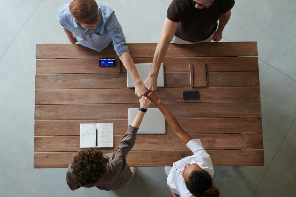 Four people giving each other fist bump across the table.